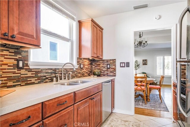 kitchen with light tile patterned floors, tasteful backsplash, light countertops, stainless steel dishwasher, and a sink