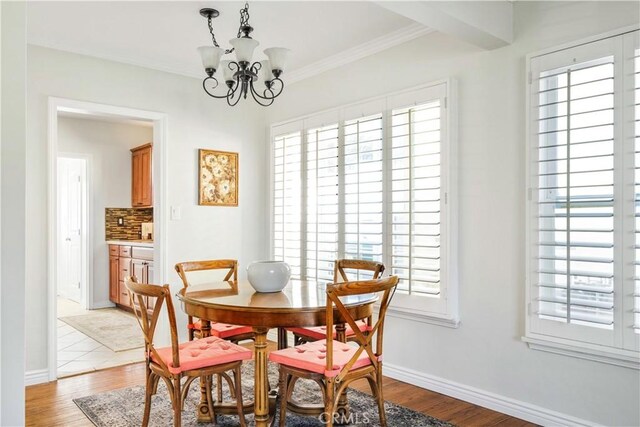 dining space featuring light wood-style flooring, baseboards, a notable chandelier, and ornamental molding