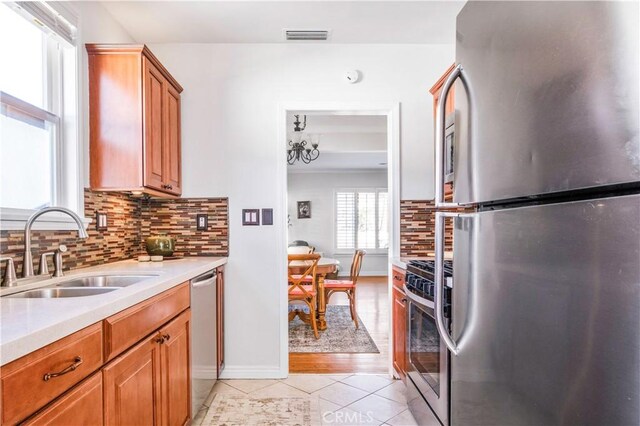 kitchen featuring light tile patterned floors, stainless steel appliances, a sink, light countertops, and decorative backsplash