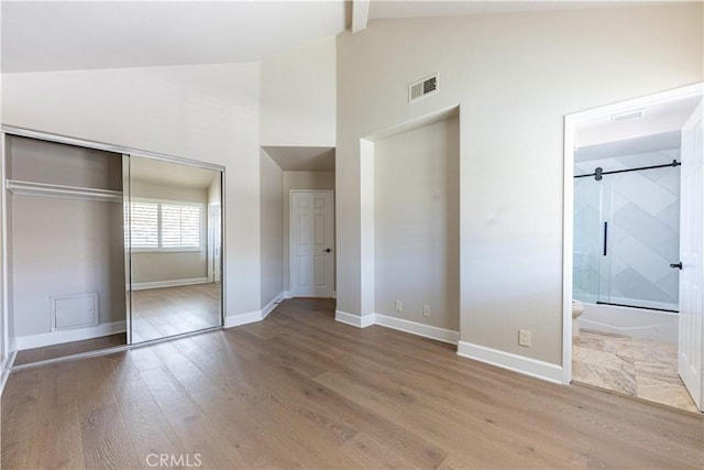 unfurnished bedroom featuring hardwood / wood-style floors, beamed ceiling, a closet, high vaulted ceiling, and ensuite bathroom