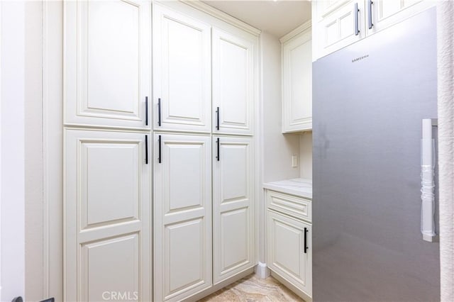 kitchen with white cabinetry, stainless steel fridge, and light stone counters