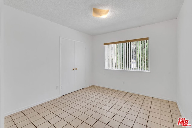 empty room with a textured ceiling and light tile patterned floors