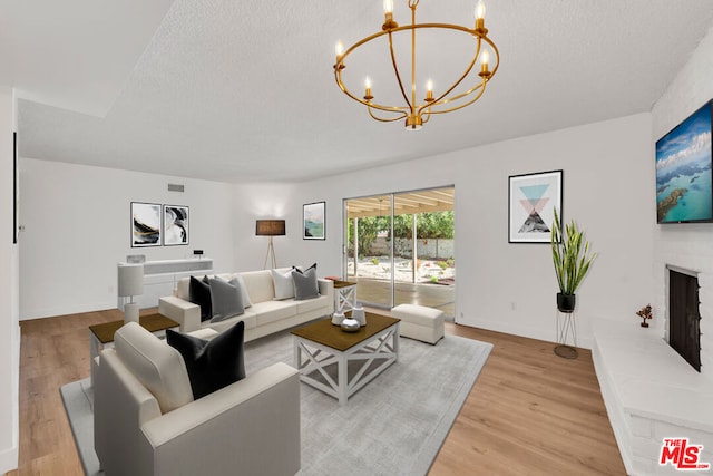 living room with a brick fireplace, an inviting chandelier, a textured ceiling, and light hardwood / wood-style flooring