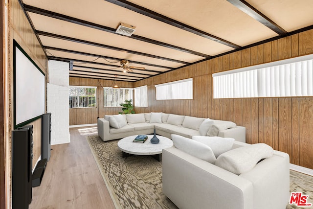 living room with light wood-type flooring, ceiling fan, beam ceiling, and wooden walls