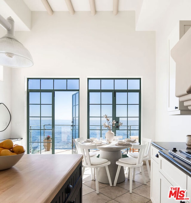 kitchen with beamed ceiling, a high ceiling, white cabinetry, a water view, and light tile patterned floors