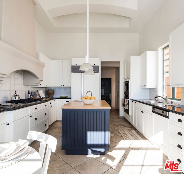 kitchen featuring a high ceiling, a kitchen island, white cabinetry, built in appliances, and sink