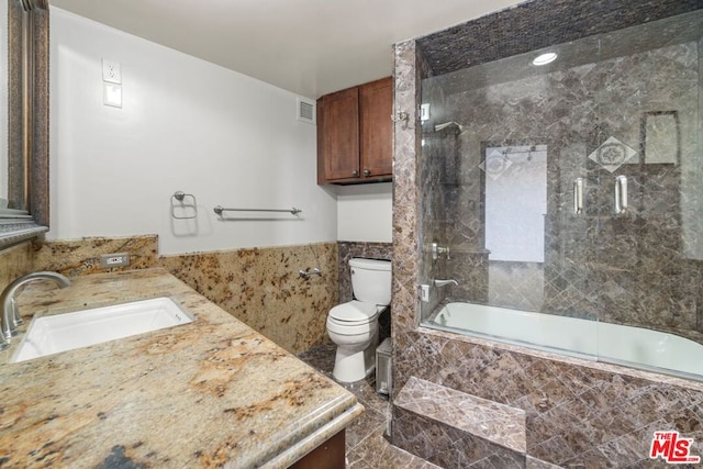 full bathroom with combined bath / shower with glass door, vanity, tile walls, and toilet