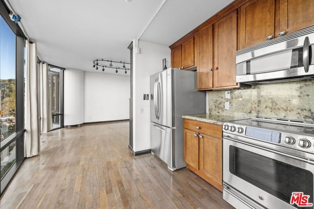 kitchen with tasteful backsplash, light hardwood / wood-style floors, appliances with stainless steel finishes, light stone counters, and rail lighting