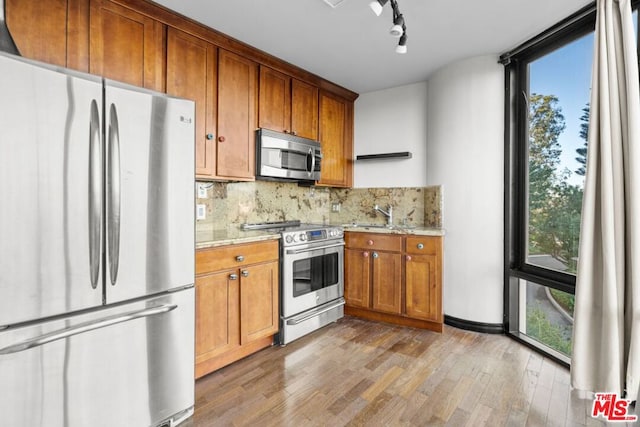 kitchen featuring tasteful backsplash, light hardwood / wood-style flooring, appliances with stainless steel finishes, track lighting, and light stone counters