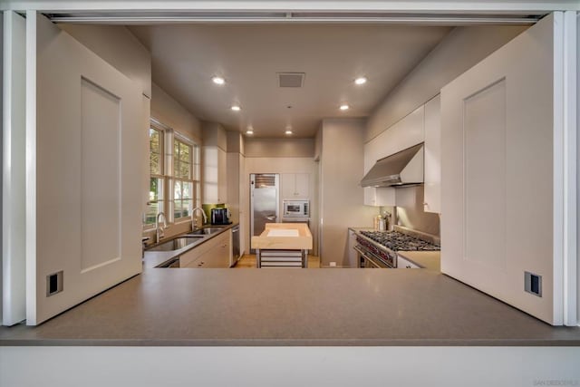 kitchen featuring kitchen peninsula, stainless steel appliances, wall chimney range hood, and sink