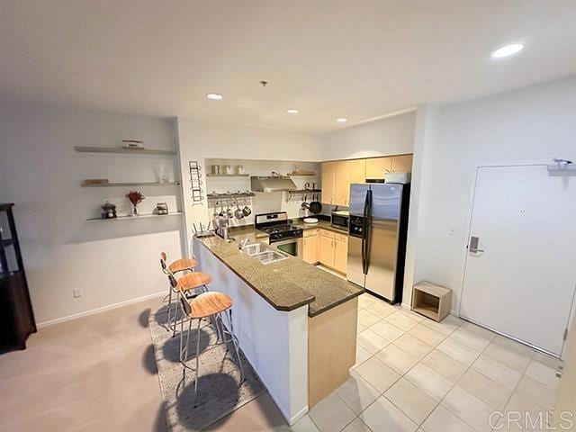 kitchen with exhaust hood, light tile patterned floors, kitchen peninsula, a breakfast bar area, and appliances with stainless steel finishes