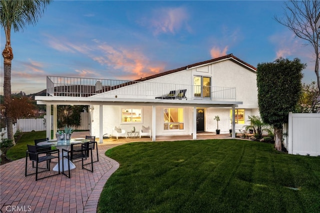 back house at dusk featuring a lawn, a patio area, and a balcony