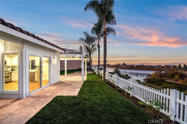 yard at dusk featuring a water view, a patio area, and a balcony