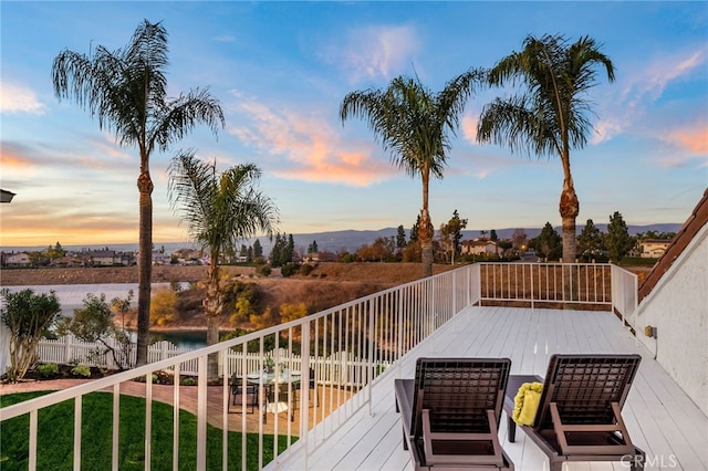 deck at dusk featuring a mountain view and a lawn