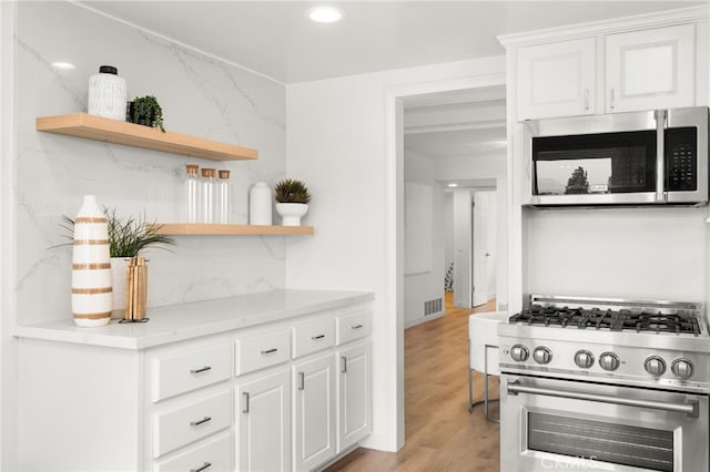 kitchen with light wood-type flooring, stainless steel appliances, white cabinetry, and tasteful backsplash