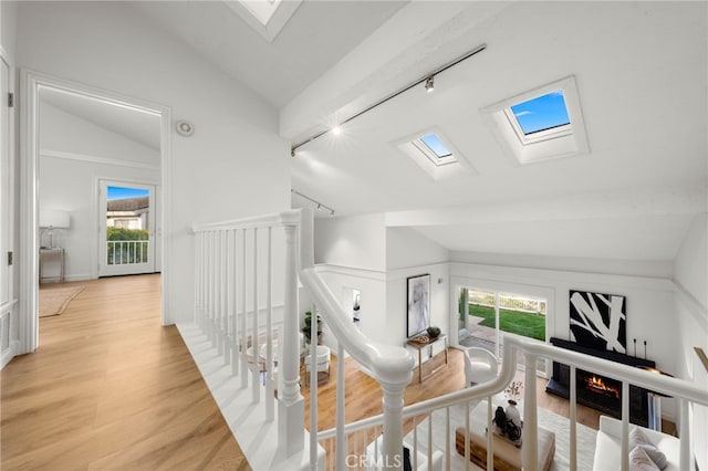 corridor featuring light hardwood / wood-style floors, vaulted ceiling with skylight, rail lighting, and a healthy amount of sunlight