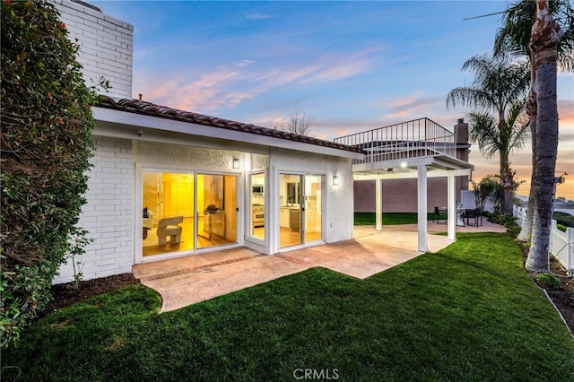 back house at dusk featuring a patio area and a yard