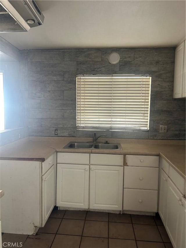 kitchen with white cabinets, light countertops, a sink, dark tile patterned flooring, and a peninsula