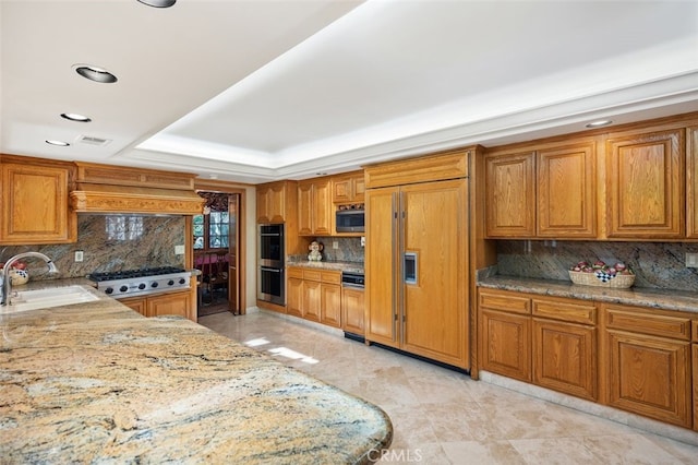 kitchen featuring a raised ceiling, backsplash, built in appliances, and sink