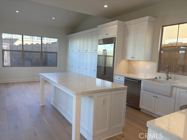 kitchen with light hardwood / wood-style floors, appliances with stainless steel finishes, sink, white cabinets, and a center island