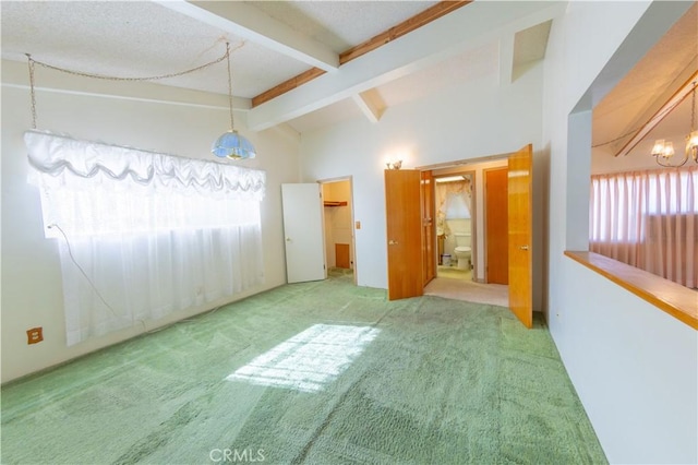 carpeted empty room with an inviting chandelier and vaulted ceiling with beams