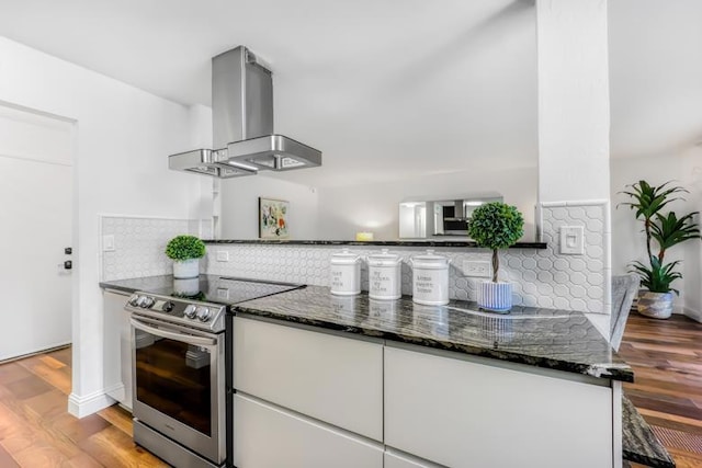 kitchen featuring hardwood / wood-style floors, white cabinetry, dark stone counters, island exhaust hood, and electric stove