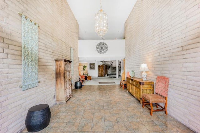 corridor featuring a towering ceiling, brick wall, and a chandelier