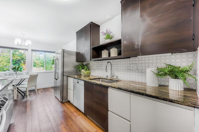 kitchen with sink, dark stone countertops, a chandelier, white dishwasher, and light hardwood / wood-style flooring