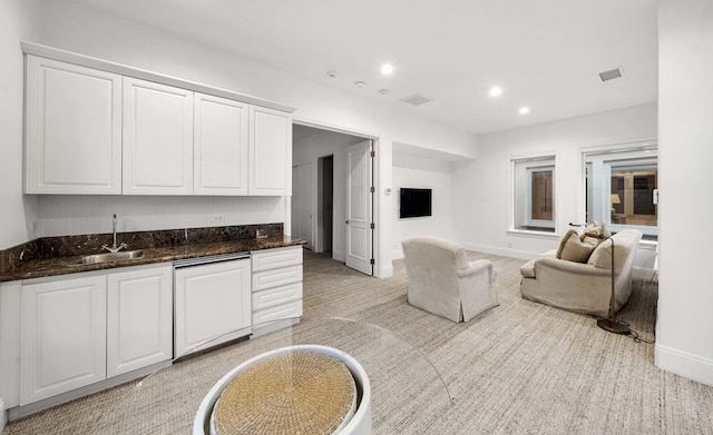 kitchen featuring white cabinetry, light carpet, dark stone counters, sink, and white dishwasher