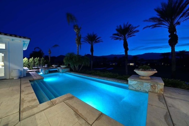 pool at night with a mountain view, an in ground hot tub, and a patio