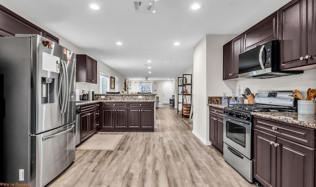 kitchen with kitchen peninsula, stainless steel appliances, light stone countertops, dark brown cabinets, and light wood-type flooring