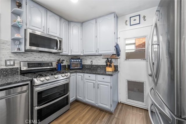 kitchen with hardwood / wood-style floors, appliances with stainless steel finishes, white cabinetry, dark stone counters, and backsplash