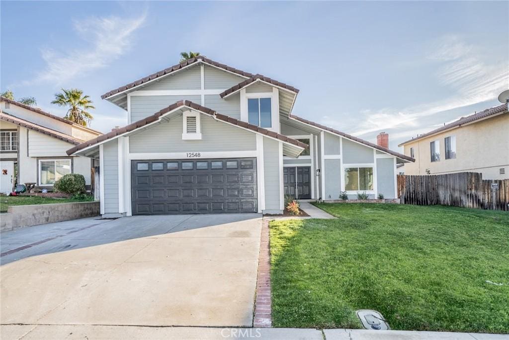 view of front facade featuring an attached garage, fence, driveway, a tiled roof, and a front lawn