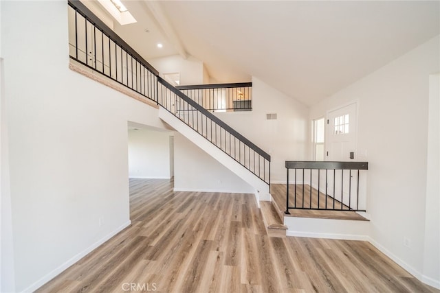 stairway with hardwood / wood-style flooring, high vaulted ceiling, and a skylight