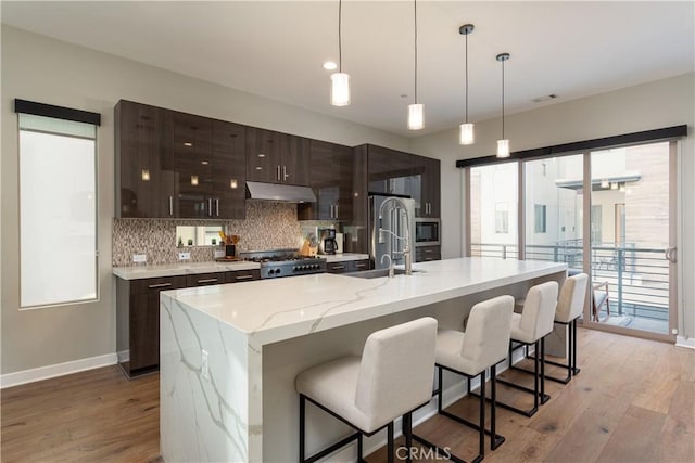 kitchen with an island with sink, dark brown cabinets, range, light stone counters, and sink