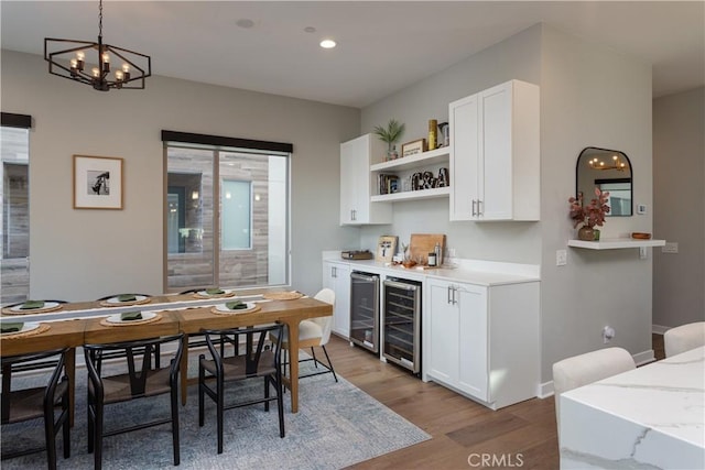 bar featuring wine cooler, decorative light fixtures, light wood-type flooring, and white cabinetry