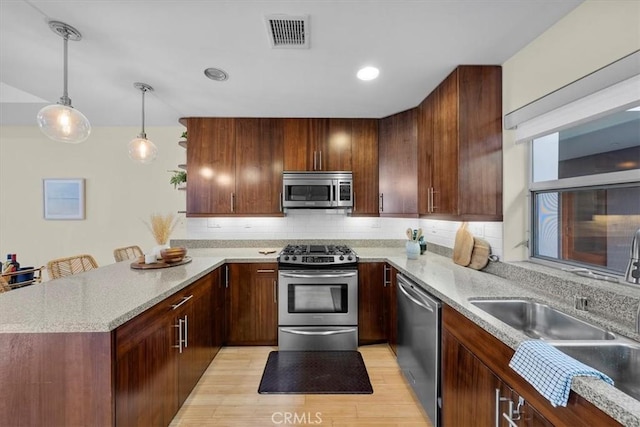 kitchen with sink, stainless steel appliances, pendant lighting, light hardwood / wood-style floors, and a breakfast bar area