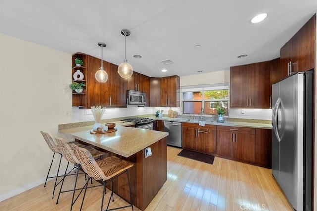 kitchen with kitchen peninsula, appliances with stainless steel finishes, a breakfast bar, decorative light fixtures, and light hardwood / wood-style flooring