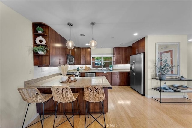 kitchen featuring hanging light fixtures, kitchen peninsula, a kitchen bar, decorative backsplash, and appliances with stainless steel finishes