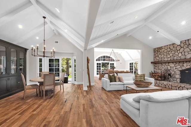 living room featuring an inviting chandelier, hardwood / wood-style floors, a stone fireplace, and beamed ceiling