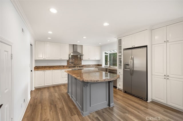 kitchen with white cabinetry, appliances with stainless steel finishes, a kitchen island, and wall chimney range hood