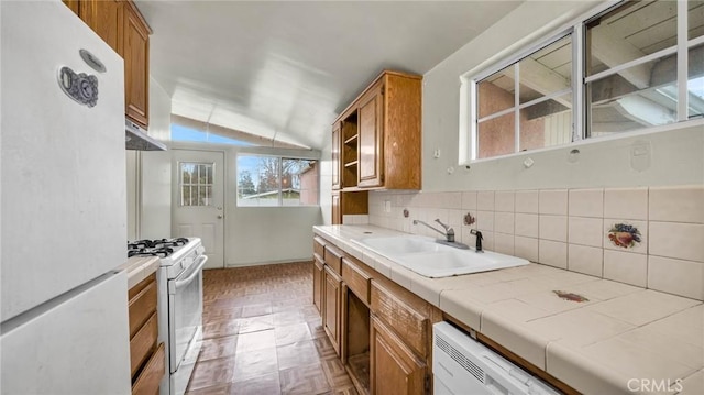 kitchen with white appliances, decorative backsplash, sink, tile countertops, and vaulted ceiling