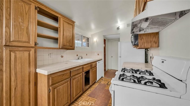 kitchen with light parquet floors, tile counters, white appliances, range hood, and sink