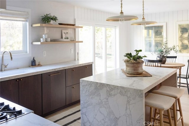 kitchen with decorative light fixtures, a kitchen bar, sink, and dark brown cabinetry