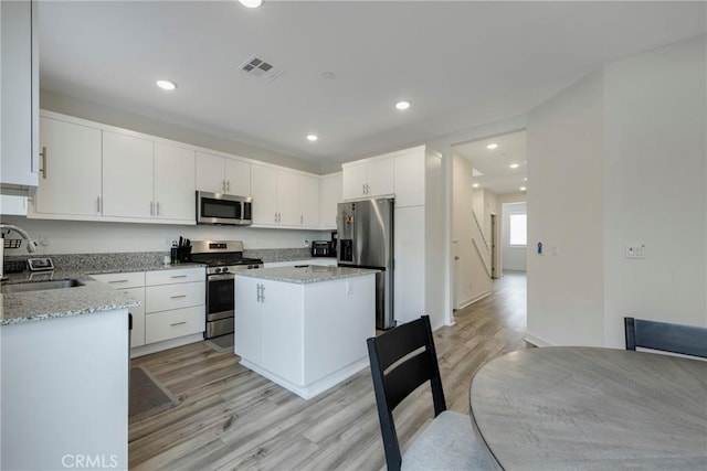 kitchen with light stone countertops, white cabinets, appliances with stainless steel finishes, a kitchen island, and sink