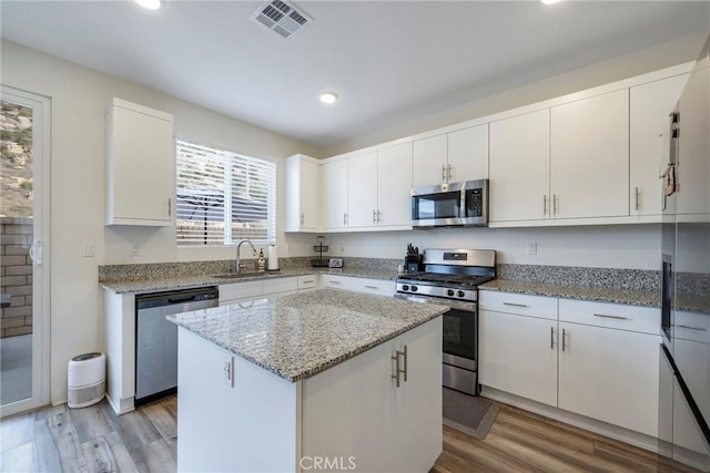 kitchen with a kitchen island, sink, white cabinetry, appliances with stainless steel finishes, and light stone counters