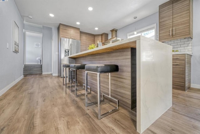 bar with decorative backsplash, stainless steel fridge with ice dispenser, pendant lighting, and light hardwood / wood-style flooring