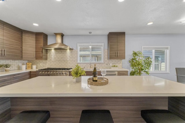 kitchen with a breakfast bar area, a healthy amount of sunlight, tasteful backsplash, stove, and wall chimney exhaust hood