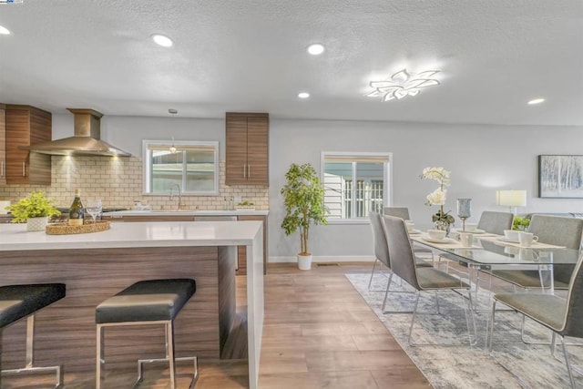 kitchen featuring stainless steel gas stovetop, tasteful backsplash, wall chimney range hood, light hardwood / wood-style flooring, and sink