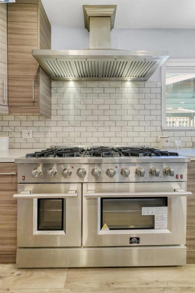 kitchen with double oven range, backsplash, and wall chimney exhaust hood